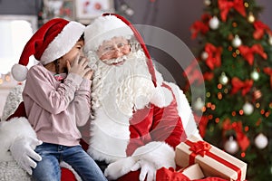 Little girl whispering in authentic Santa Claus`