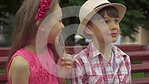 Little girl whispers in boy`s ear on the bench