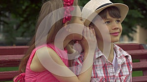 Little girl whispers in boy`s ear on the bench