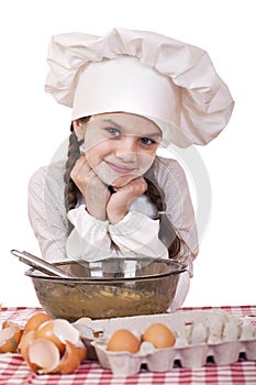 Little girl in a white apron breaks near the plate with eggs