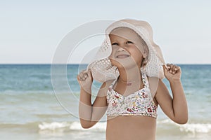 Little girl in a white beach hat and bikini by the sea