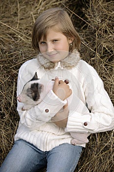 Little girl in a white blouse sits and holds a piglet and smiles. Lifestyle portrait