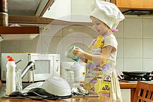 Little girl in white chef hat is washing dishes.