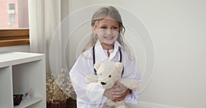 Little girl in white coat holding fluffy toy pose indoor