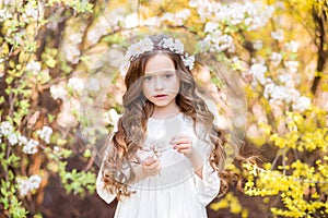 Little girl in a white dress on a background of yellow flowers. Spring photo with a beautiful girl. A child with a wreath of