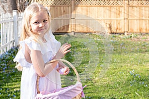 Little girl in white dress collecting Easter eggs in the backyard