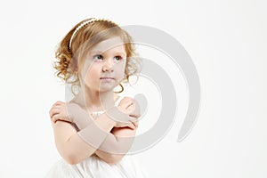Little girl in white dress with crossed arms looks
