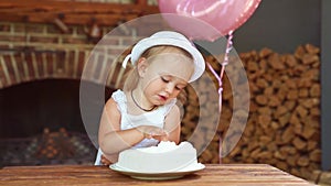 Little girl in white dress and hat, festive eats with his hands cake.