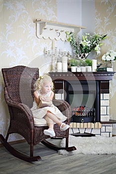 Little girl in white dress sits in wicker rocking