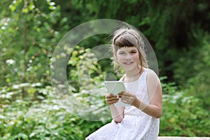 Little girl in white dress smiles and holds tablet pc