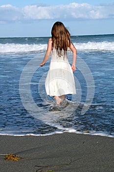 Little Girl in White Dress Steps Into Ocean as Wave Rolls In