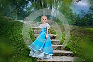 Little girl with white hair in a blue retro dress. Princess from a fairy tale stands on the stairs