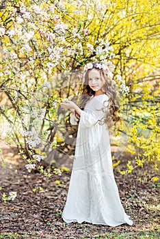 Little girl in a white long dress on a background of yellow flowers. Spring photo with a beautiful girl