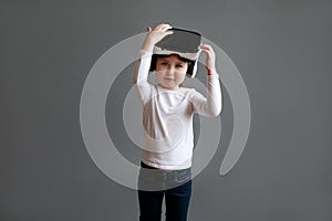 Little girl in white long sleeve shirt wearing virtual reality glasses over grey background