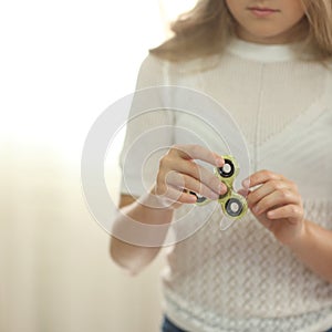 Little girl in white shirt playing with green fidget spinner in bright room