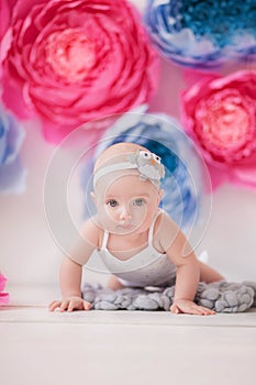 Little girl in a white suit in a white room with bright pink and blue paper flowers, baby photo session