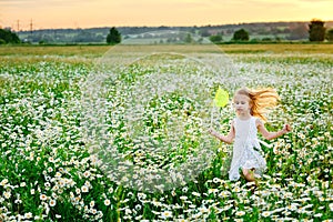 A little girl in a white sundress runs through a field of flowering daisies and holds a net for catching insects