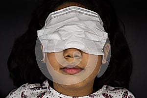 Little girl in white surgical mask covers her eyes and leaves her nose and mouth free. Concept of ignorance and happiness in the