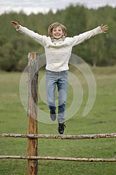 Little girl in white sweater and blue jeans is jumping off the fence. Lifestyle portrait