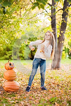 Little girl in a white sweater and jeans on a background of green textural natural background. A girl dancing with pumpkins near t