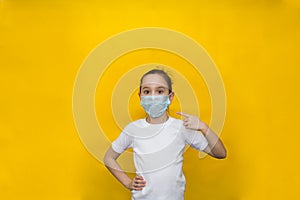 Little girl in a white t-shirt and protective mask points her finger at the mask. Protection against coronavirus