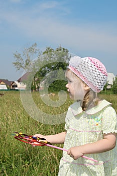 Little girl with windmill looks away at meadow