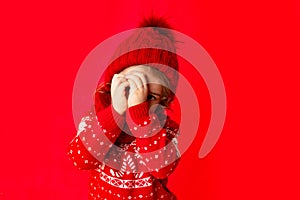 A little girl in winter clothes spies on a red background. New year`s concept