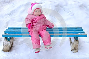 Little girl in winter outerwear sit on bench.