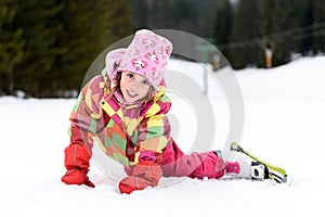 Little girl in winter outfit fell while skiing.