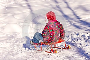 A little girl on a winter walk rides down a snow slide in a city park.