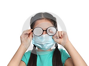 Little girl wiping foggy glasses caused by wearing medical face mask on white background. Protective measure during coronavirus