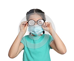 Little girl wiping foggy glasses caused by wearing medical face mask on white background. Protective measure during coronavirus