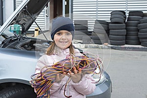 Little girl with a wire in her hands works in a car service. Repair service