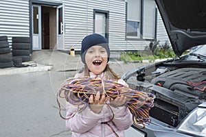 A little girl with a wire in her hands works in the garage.  Car service