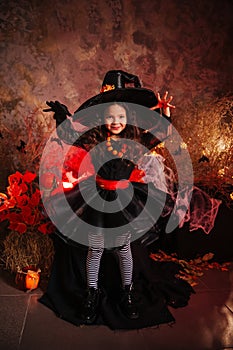 A little girl in a witch costume on a gloomy background scares people. Getting ready for All Saints Day. Halloween costume