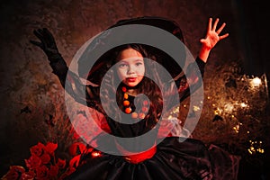 A little girl in a witch costume on a gloomy background scares people. Getting ready for All Saints Day. Halloween costume