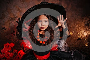 A little girl in a witch costume on a gloomy background scares people. Getting ready for All Saints Day. Halloween costume