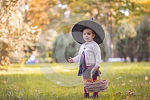 Little girl in witch costume at Halloween in autumn park with basket full of yellow leaves. Childhood, helloween