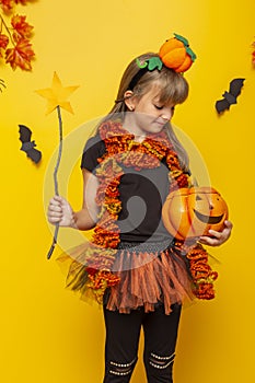 Little girl in witch costume for Halloween holding magic wand and pumpkin