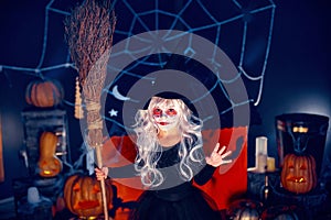 Little girl in witch costume holding broom in hand and scaring on background decor Halloween party