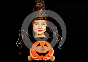 A little girl in a witch costume, holding a pumpkin, shot on a black background. Happy Halloween concept.