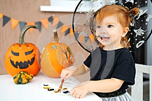 a little girl in a witch costume paints pumpkins for Halloween at home, the concept of children& x27;s creativity