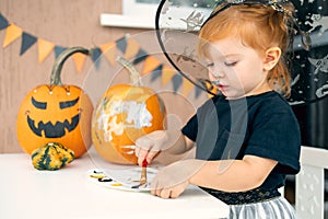 a little girl in a witch costume paints pumpkins for Halloween at home, the concept of children& x27;s creativity