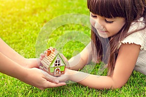 little girl and a woman hands holding small house on a background of green grass