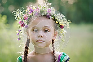 Little girl in a wreath of wild flowers in summer