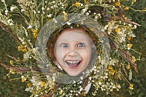 Little girl with a wreath of wildflowers looks at the camera