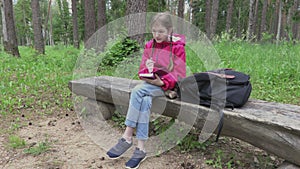 Little girl writing and thinking on bench in park