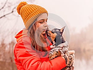 A little girl of 10-11 years old in an orange jacket with her pet, a Chihuahua dog, in nature