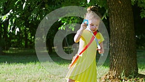 A little girl in yelllow dress playing with soap bubbles in the midow. Outdoor having fun.