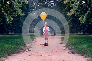 Little girl with a yellow balloon in her hands in a dark forest